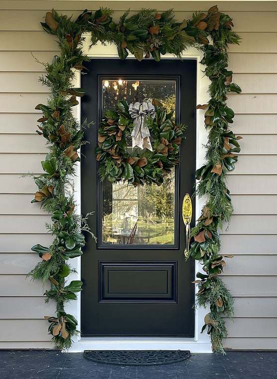 Fresh magnolia and cedar garland framing a front door with a matching magnolia wreath