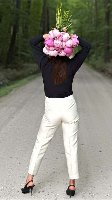An armful of fresh pink garden peonies held high on a wooded gravel road