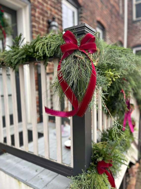Fresh evergreen garland swags with red velvet bows on a porch railing