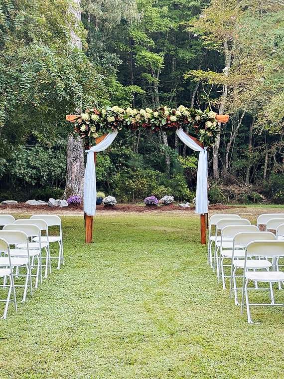 Wooden ceremony arch with magnolia and green hydrangea garland, white draping and rows of white chairs