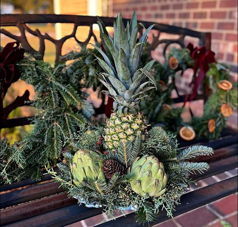Williamsburg-style centerpiece with pineapple and artichokes on a garden bench