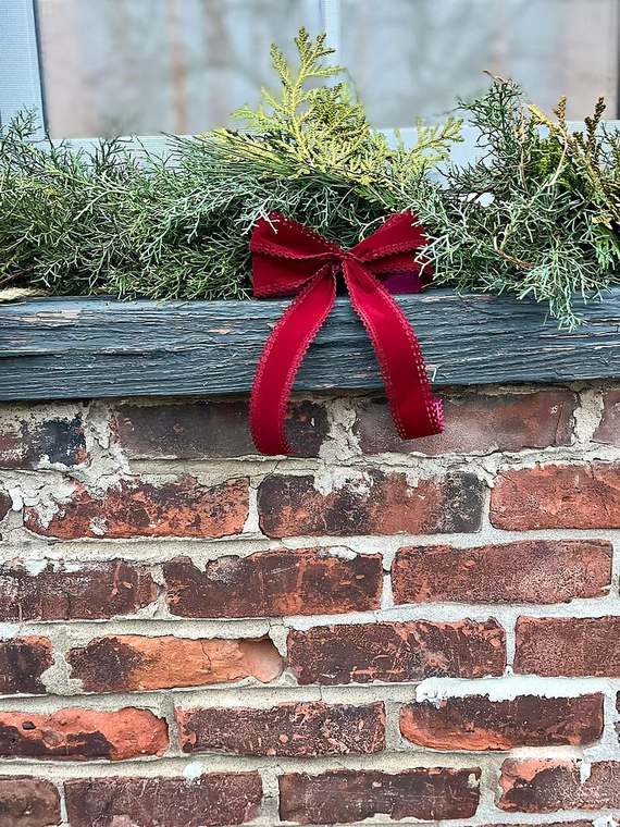 Window box filled with fresh greenery and a red velvet bow